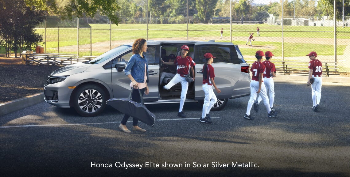 Side view of a woman and young baseball players around a 2026 Honda Odyssey Elite in Solar Silver Metallic.